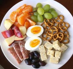 a white plate topped with fruit and crackers next to an egg, oranges, grapes