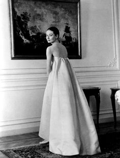 an old photo of a woman in a long dress standing next to a painting on the wall