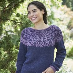 a woman standing in front of a tree wearing a purple and blue sweater with an intricate design