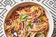 a white bowl filled with pasta and sauce on top of a table cloth next to a fork