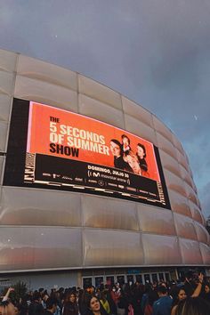 a crowd of people standing in front of a building with a large screen on it