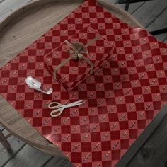 a red and white checkered table cloth with scissors on it next to a wrapped present