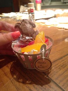 a person holding up a cupcake with chocolate frosting and fruit in it on a wooden table