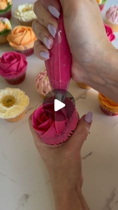 a woman is decorating cupcakes with pink frosting and flowers on them