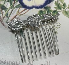 This is a unique handmade small, silver hair accessory, up cycled from a sterling silver floral brooch. This pre owned up cycled sterling silver hair comb features a small sprig of flowers in an Art Nouveau style. The perfect bridal hair accessory for a vintage inspired wedding.  The reverse is fully hallmarked London 1990.  The brooch pin is still intact and has been wired onto the hair comb, so that you could remove and wear again as a brooch if you wish.  As a  preloved, piece will show slight signs of wear relative to its age.  Approximate measurements  Length 5 cm Brooch Length 5 cm  Total comb height 4 cm This item will arrive in a gift box.  Postage will be combined for purchases made in the same transaction. Silver Hair Accessory, Floral Hair Comb, Silver Hair Comb, Theme Vintage, Silver Hair Pin, Floral Hair Combs, Floral Accessories Hair, Flower Hair Comb, Vintage Inspired Wedding