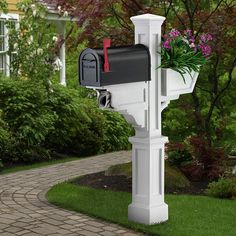 a white mailbox with flowers in it on the side of a brick path next to a house