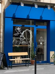 a blue store front with a wooden bench in the foreground and potted plants outside