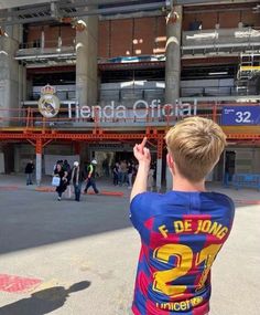 a young boy standing in front of a stadium holding his hand up to the sky