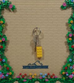 a lego keychain hanging on a brick wall with flowers and vines around it