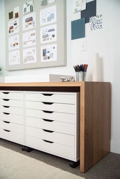 a white dresser with lots of drawers in the corner next to a wall mounted poster