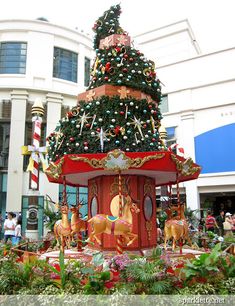 there is a christmas tree on display in the middle of this town square with people walking around it