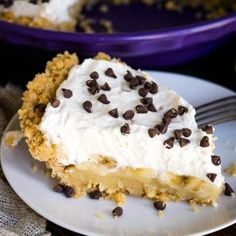 a piece of cake with white frosting and chocolate chips is on a plate next to a fork