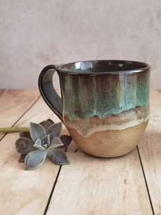 a coffee cup sitting on top of a wooden table next to a succulent plant