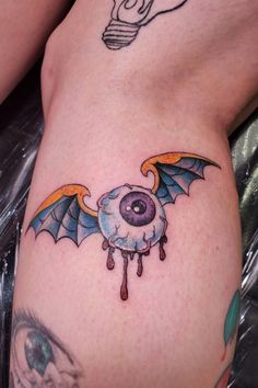 a bat tattoo on the side of a woman's leg with an eyeball