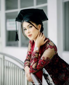 a woman in a graduation cap and gown leaning against a railing with her hand on her shoulder