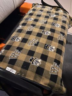 a black and white checkered luggage bag sitting on top of an orange chair next to a pillow