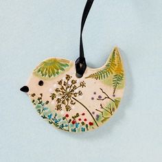 a ceramic bird ornament hanging from a cord on a blue surface with flowers and leaves