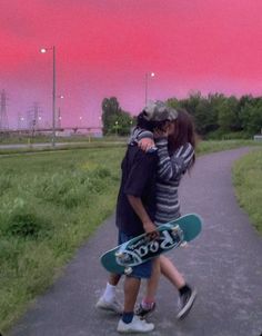 two people walking down a path with skateboards in their hands and one person hugging the other