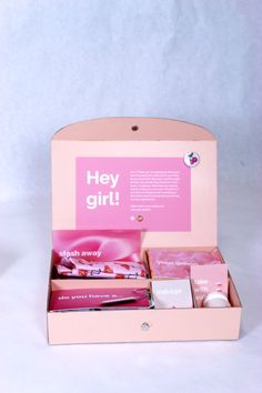 an open pink box with various items inside on a white tableclothed background and the words hey girl written in it