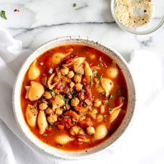 a bowl of pasta and bean soup on a white tablecloth next to a spoon