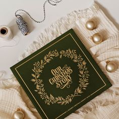 a green christmas card sitting on top of a white blanket next to some gold ornaments