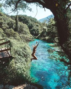 a person jumping into the water from a bridge over some blue river with green trees