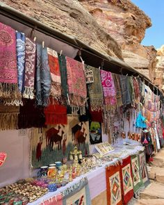 an outdoor market with lots of colorful fabrics and rugs hanging from the side of it