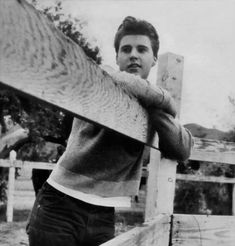 an old photo of a man leaning on a fence