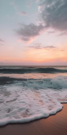 an ocean beach with waves coming in to shore and the sun setting on the horizon