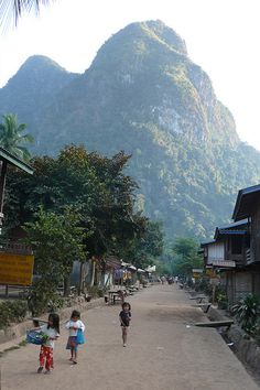 two children are walking down the street in front of some houses with mountains in the background