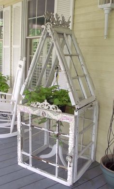 a house made out of old windows with plants growing in it on the front porch