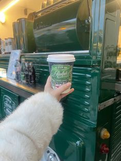 a person holding up a cup of coffee in front of a green truck with an oven