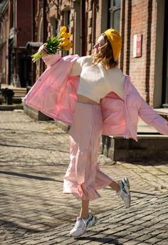 a woman is walking down the street with flowers in her hand