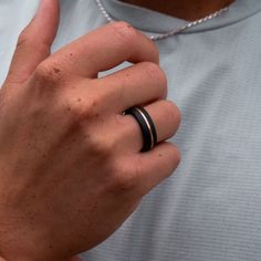 a man wearing a black ring with two bands on his fingers, standing in front of a white shirt