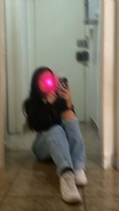 a person sitting on the floor with a cell phone in their hand and a red light coming from behind them