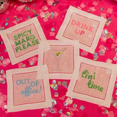 four embroidered cocktail napkins on a table with confetti and pink tissue paper