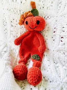 an orange crocheted stuffed animal laying on top of a white knitted blanket