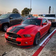 a red mustang parked in a parking lot next to other cars