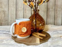 a crocheted coffee cup cozys up next to a vase with dried flowers