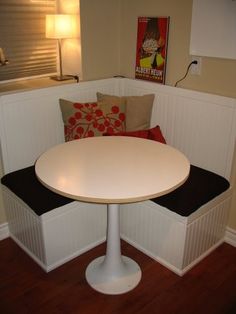 a white table and bench in a room with wood flooring on one side and red pillows on the other