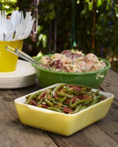 green beans are in a yellow bowl on a picnic table with other dishes and utensils