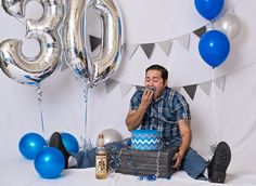 a man sitting on the floor in front of balloons and presents for his 30th birthday