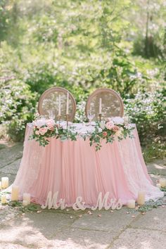 a table with two chairs and flowers on it in front of some candles, surrounded by greenery