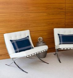 two white chairs sitting next to each other in front of a wall with wood paneling