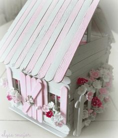 a pink and white wooden doll house with flowers around the front porch door, window and shutters