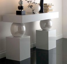 a white table with two vases on top of it next to a lamp and some books