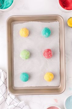 colorful play dough on a baking tray surrounded by bowls of colored powder and spoons