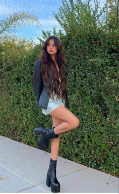 a woman in short shorts and jacket posing for the camera with her legs crossed, wearing high heeled boots