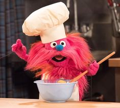 the sesame street character is mixing food in a bowl with chopsticks and wearing a chef's hat