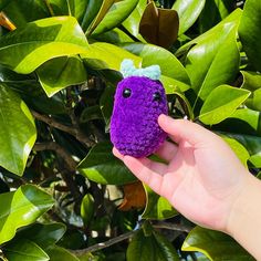 a hand holding a purple stuffed animal on top of a tree filled with green leaves